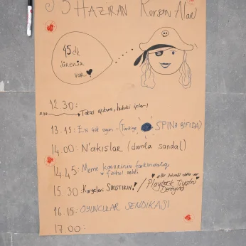 Bu çalışmada, açık kahverengi bir zemin üzerinde çeşitli yazılar ve çizimler yer alıyor. Üst kısmın sol tarafında, sayılar ve harflerle "5 HAZİRAN" ve "Korsan Alan" yazılı. Bu yazıların yanında, bir balon içinde "45 dk süreniz var!" ifadesi bulunuyor. Üst orta kısımda, bir korsan şapkalı ve göz bandı olan bir karakter resmi var. Alt kısımda ise saat dilimlerine göre sıralanmış etkinlikler belirtilmiş. Saat 12:30'dan başlayarak, 17:00'ye kadar sürecek farklı aktivitelerin adları belirtilmiş, örneğin "Takas aşkına, hukuki işler!" ve "N'akışlar (damla sandal)". Ek olarak, "Meme konseyinin farkındalığı ve fiziksel anlatı" gibi etkinlikler içerikte yer almakta. Çeşitli simgeler ve işaretlerle zenginleştirilmiş. Sol altta bir kalem duruyor.